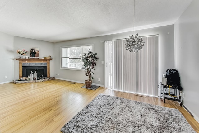 living room with a notable chandelier, a textured ceiling, hardwood / wood-style flooring, and a tile fireplace