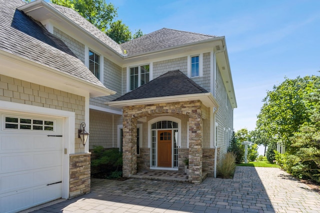 property entrance with a garage, roof with shingles, and stone siding