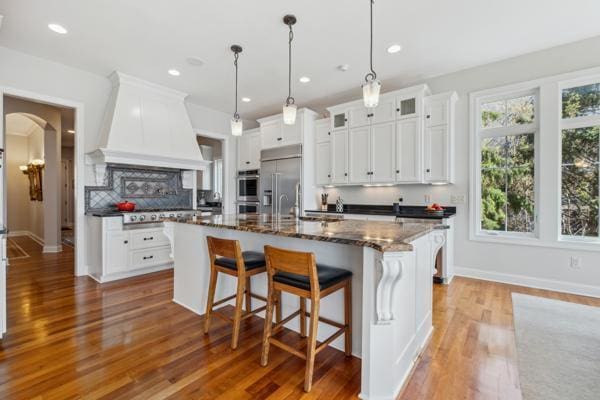 kitchen featuring appliances with stainless steel finishes, a breakfast bar, white cabinetry, wood finished floors, and custom exhaust hood
