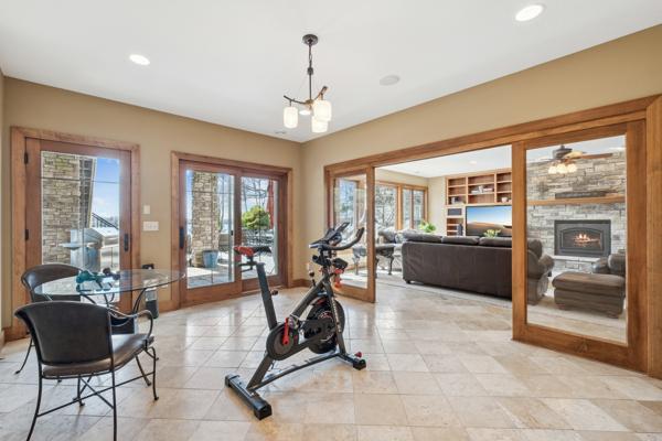 workout area featuring a stone fireplace, built in shelves, ceiling fan with notable chandelier, recessed lighting, and light tile patterned floors