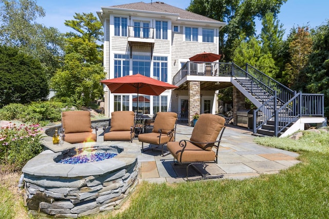 back of property with a balcony, a patio, stairs, a shingled roof, and an outdoor fire pit