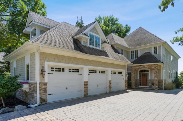craftsman-style home featuring a shingled roof, driveway, and stone siding