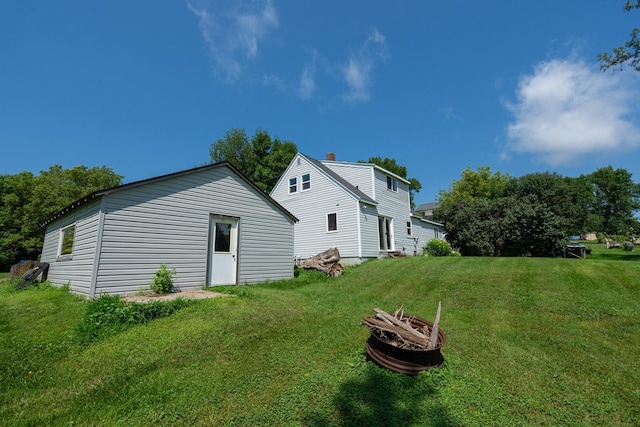 rear view of property featuring a fire pit and a lawn