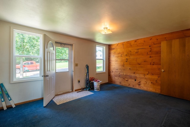 interior space featuring dark colored carpet, a wealth of natural light, and wooden walls