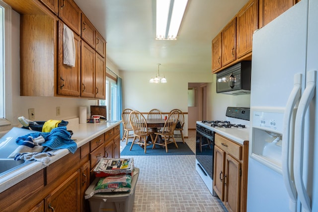 kitchen featuring gas range, decorative light fixtures, white refrigerator with ice dispenser, and an inviting chandelier