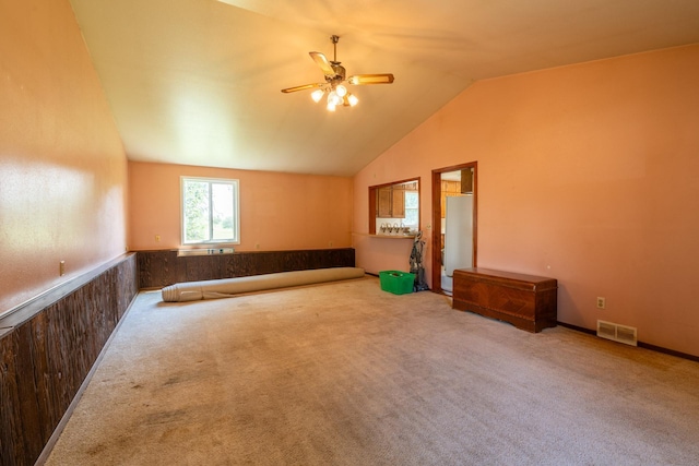 empty room featuring vaulted ceiling, wooden walls, ceiling fan, and carpet flooring