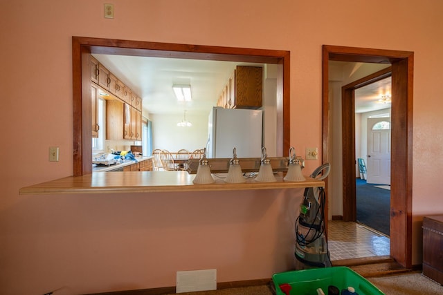 kitchen with kitchen peninsula, carpet, white fridge, and a notable chandelier