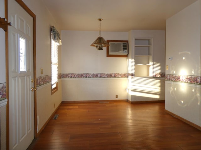 unfurnished dining area featuring a wall mounted air conditioner, built in features, and light hardwood / wood-style floors