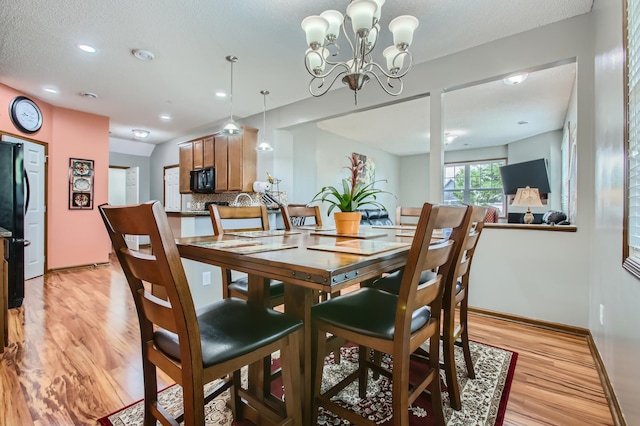 dining area featuring a textured ceiling, light wood-type flooring, and an inviting chandelier