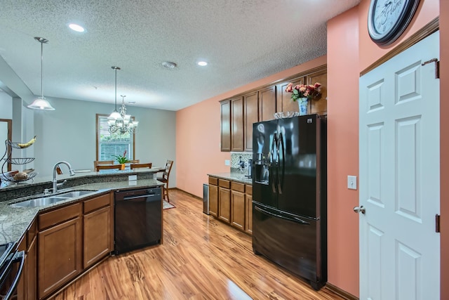 kitchen featuring light wood-type flooring, sink, black appliances, dark stone countertops, and hanging light fixtures