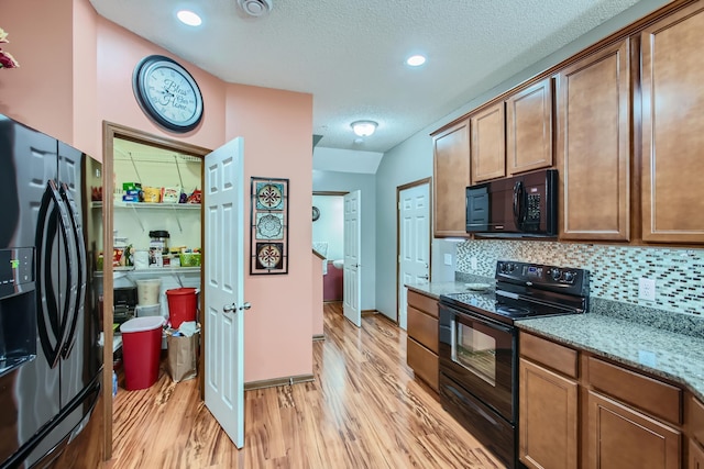 kitchen featuring backsplash, a textured ceiling, stone countertops, black appliances, and light wood-type flooring