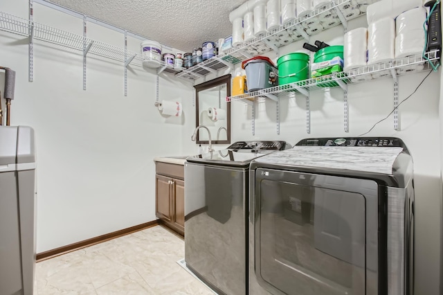 clothes washing area with washing machine and dryer, sink, cabinets, and a textured ceiling