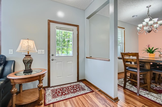 doorway featuring baseboards, a textured ceiling, a chandelier, and wood finished floors