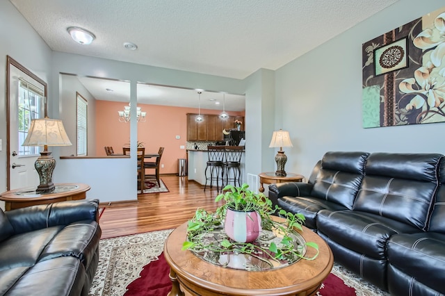 living area featuring a notable chandelier, a textured ceiling, baseboards, and wood finished floors