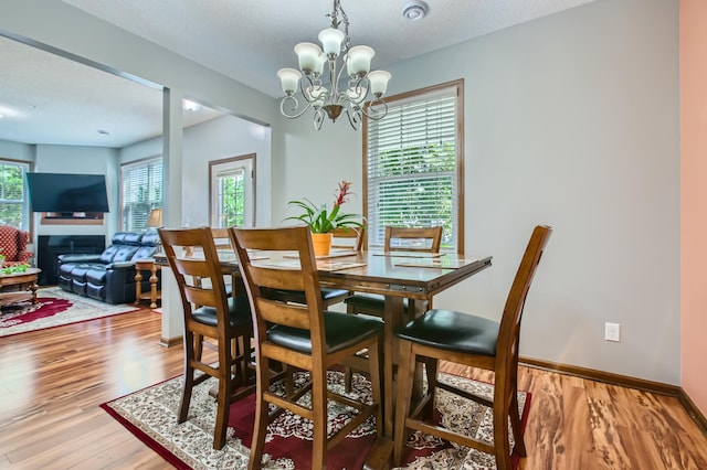 dining space with a textured ceiling, baseboards, wood finished floors, and an inviting chandelier