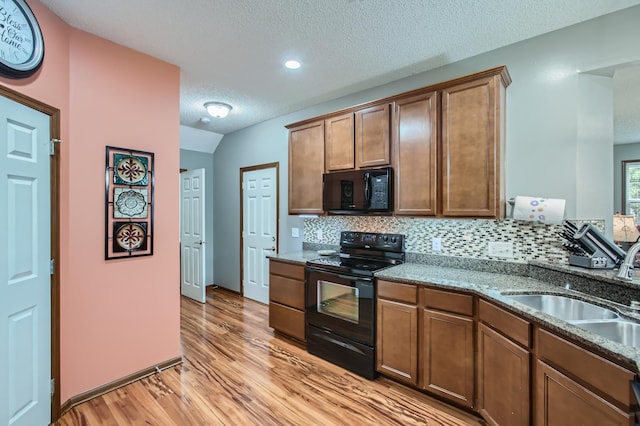 kitchen with tasteful backsplash, dark stone counters, a sink, light wood-type flooring, and black appliances