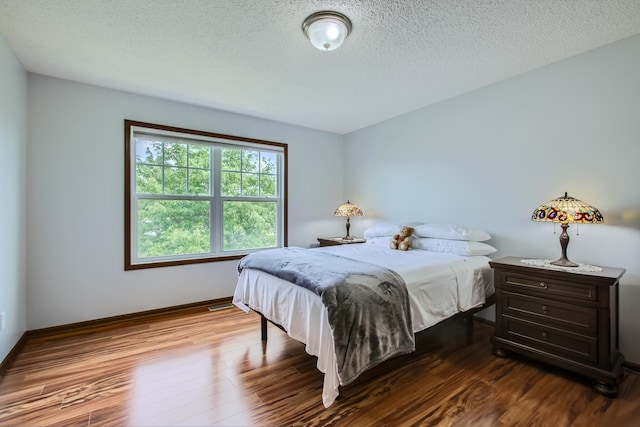 bedroom with a textured ceiling, baseboards, and wood finished floors