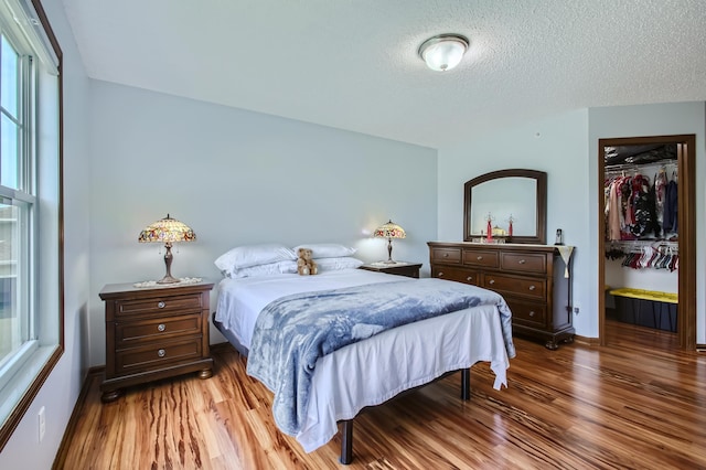 bedroom with a textured ceiling, a closet, wood finished floors, and a walk in closet