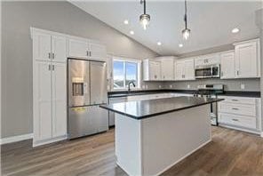 kitchen with appliances with stainless steel finishes, hardwood / wood-style flooring, vaulted ceiling, white cabinetry, and pendant lighting