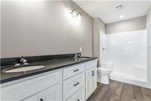 bathroom featuring double sink vanity, hardwood / wood-style floors, walk in shower, and toilet