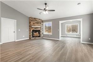 745 Hilltop Ln, Saint Croix Falls, WI 54024 - unfurnished living room with lofted ceiling, a ceiling fan, a large fireplace, wood finished floors, and baseboards