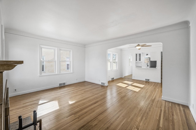 unfurnished living room featuring visible vents, wood finished floors, arched walkways, and baseboards