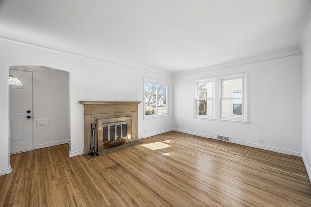 unfurnished living room featuring a fireplace with flush hearth, wood finished floors, visible vents, and baseboards