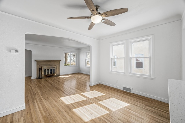 unfurnished living room featuring visible vents, arched walkways, light wood-style flooring, and a fireplace with flush hearth