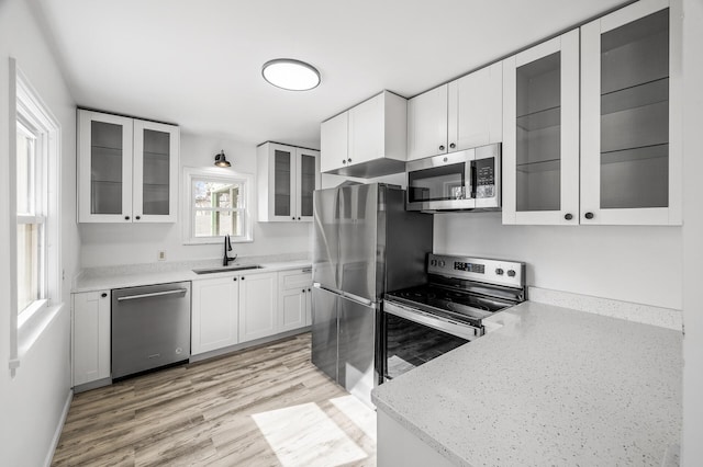 kitchen featuring light wood-type flooring, a sink, stainless steel appliances, white cabinets, and glass insert cabinets