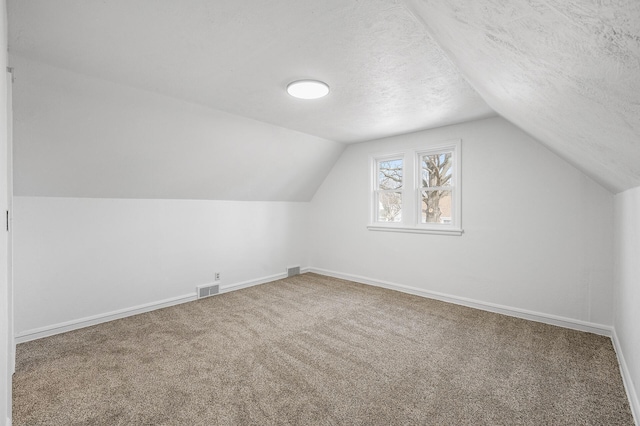 additional living space featuring visible vents, baseboards, carpet, lofted ceiling, and a textured ceiling