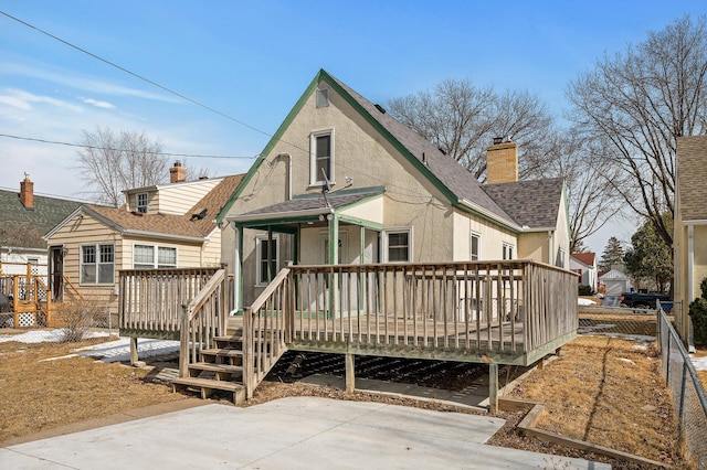 rear view of house featuring fence, a wooden deck, roof with shingles, stucco siding, and a chimney