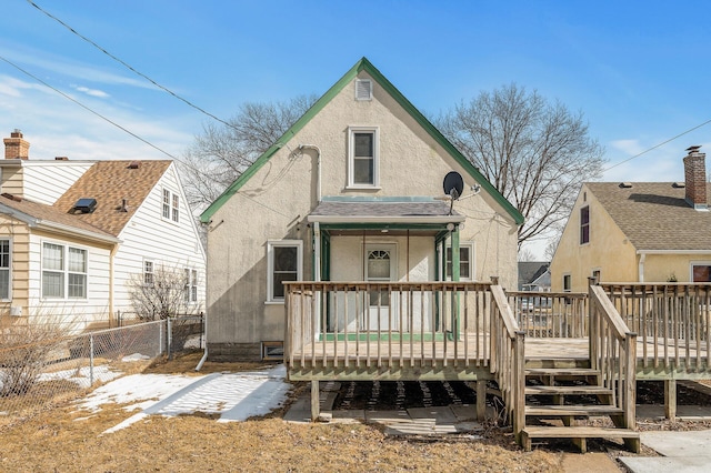 back of house with stucco siding, a shingled roof, a wooden deck, and fence