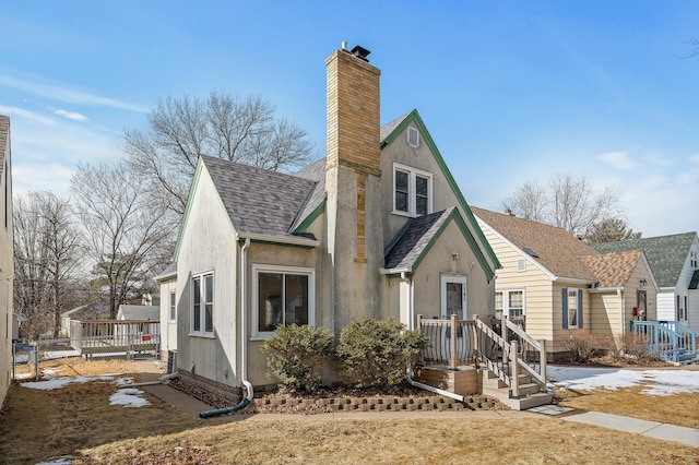 view of front of house featuring a shingled roof, stucco siding, fence, and a chimney