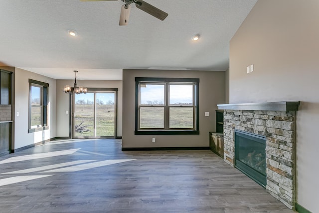 unfurnished living room with ceiling fan with notable chandelier, a stone fireplace, light wood-type flooring, and a textured ceiling