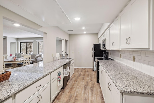 kitchen featuring stainless steel appliances, light stone countertops, decorative backsplash, and white cabinets