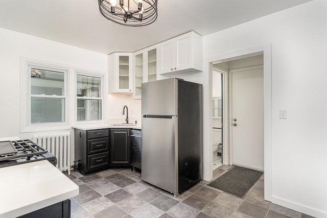 kitchen with appliances with stainless steel finishes, radiator heating unit, white cabinets, a chandelier, and sink