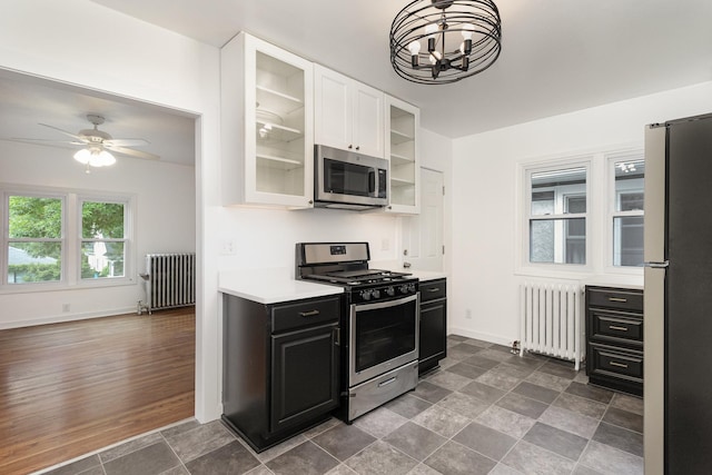 kitchen with white cabinetry, ceiling fan with notable chandelier, appliances with stainless steel finishes, and radiator heating unit