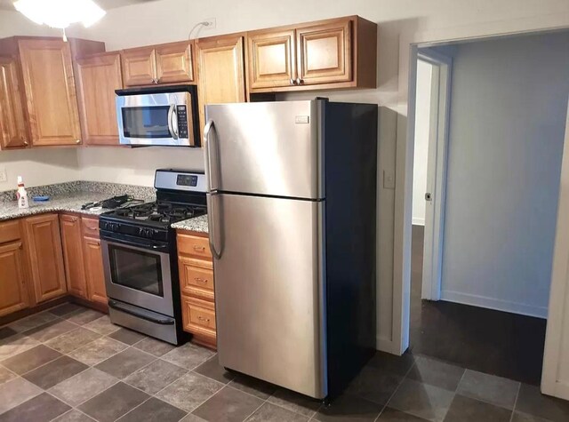 kitchen featuring dark tile patterned flooring, stainless steel appliances, and light stone countertops