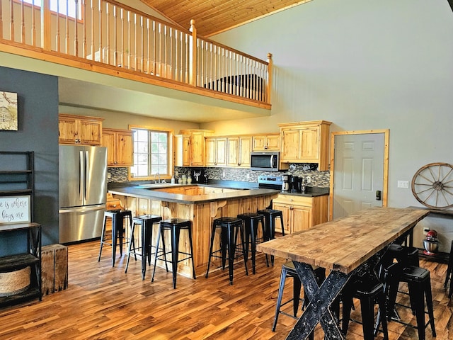 kitchen with a center island, appliances with stainless steel finishes, wood ceiling, light brown cabinets, and high vaulted ceiling