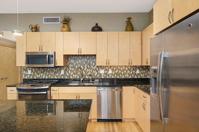 kitchen with light brown cabinetry, appliances with stainless steel finishes, dark stone countertops, and pendant lighting