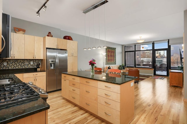 kitchen with dark stone countertops, a center island, hanging light fixtures, stainless steel fridge with ice dispenser, and light brown cabinets