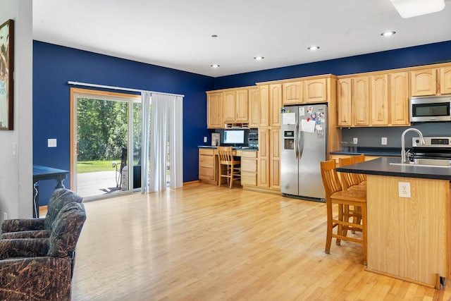 kitchen featuring dark countertops, appliances with stainless steel finishes, light brown cabinets, a sink, and light wood-style floors