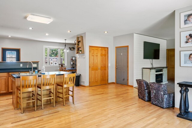 kitchen featuring open floor plan, a kitchen breakfast bar, light wood-type flooring, a large fireplace, and a center island with sink