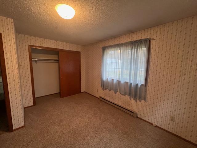 unfurnished bedroom featuring a baseboard radiator, carpet, a textured ceiling, and a closet