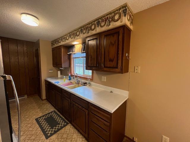 kitchen featuring dark brown cabinets, wooden walls, sink, and a textured ceiling