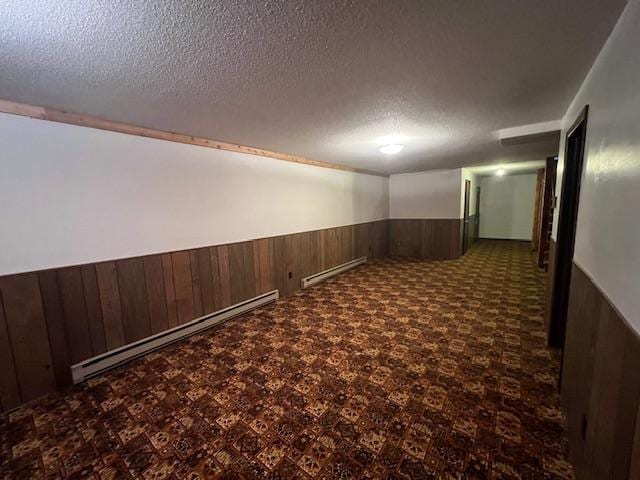 interior space featuring baseboard heating, wooden walls, and a textured ceiling