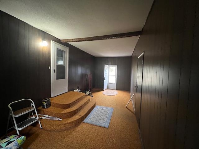 living room featuring beam ceiling, wooden walls, and carpet flooring