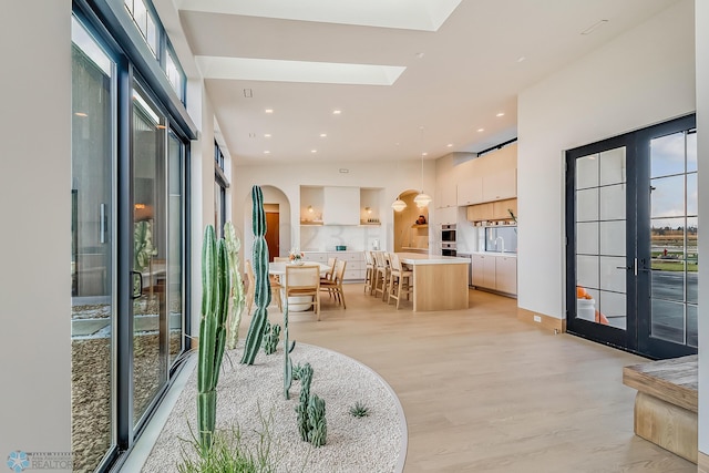 interior space featuring light wood finished floors, a skylight, arched walkways, and french doors