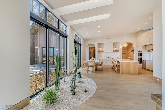 interior space with recessed lighting, a high ceiling, arched walkways, and light wood-style floors