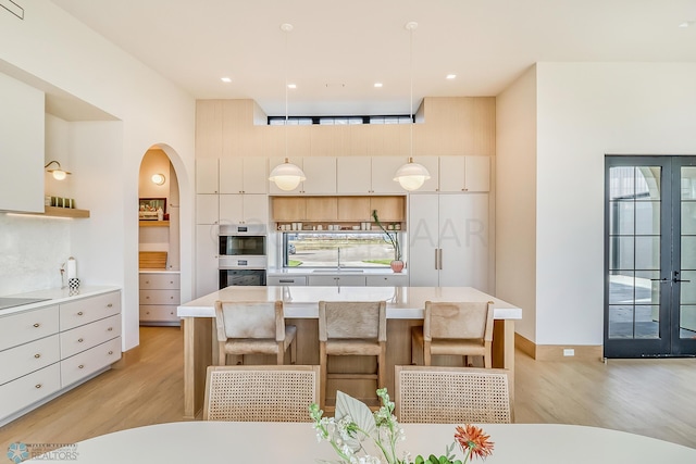 kitchen featuring light countertops, light wood-style flooring, an island with sink, and decorative light fixtures